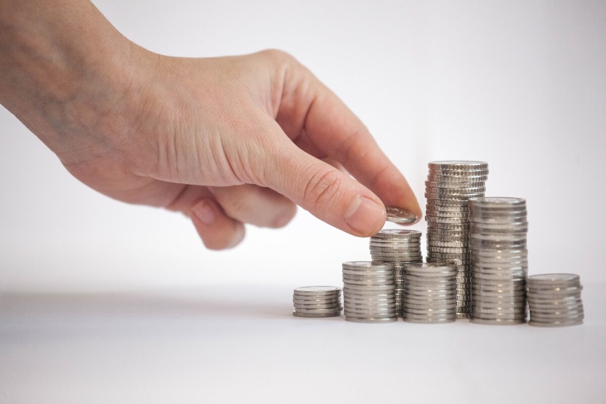 Hand stacking silver coins in ascending piles, symbolizing savings and financial growth.